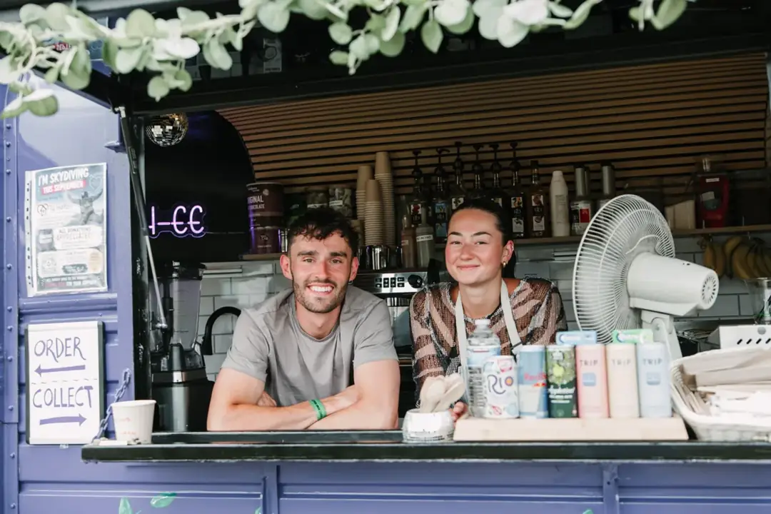 Max and Erin smiling behind the serving hatch of their purple horsebox